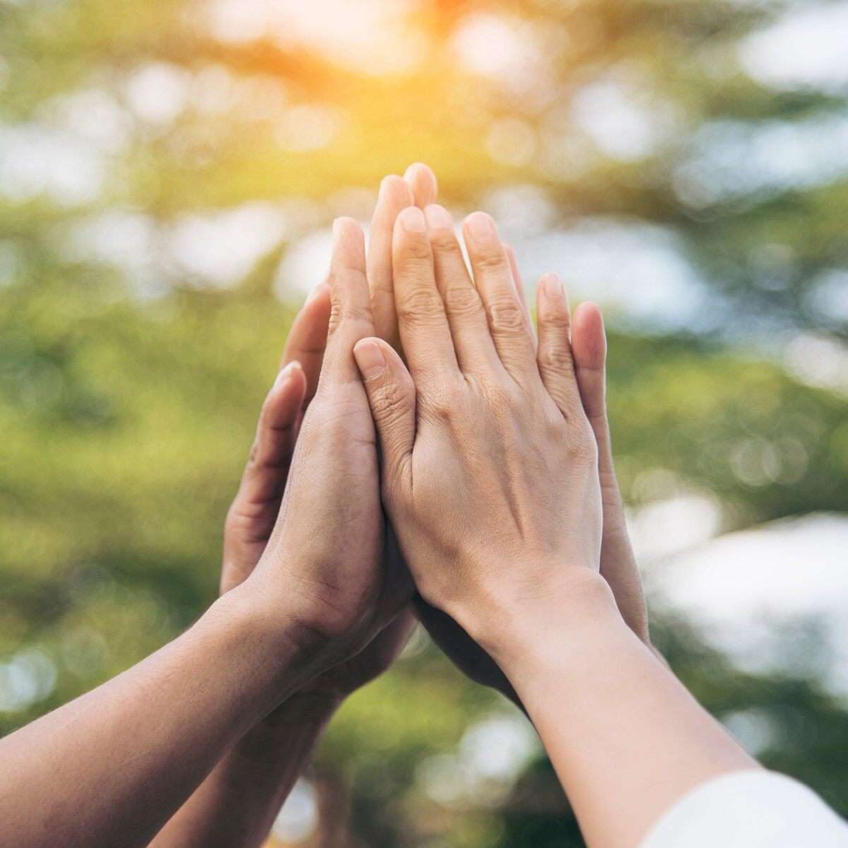 Mehrere Hände, die sich in einer Geste des gegenseitigen Zusammenhalts übereinanderlegen, im Freien bei Sonnenlicht.